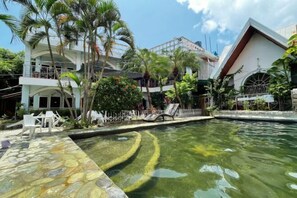 Ein Poolbereich mit ruhiger Wasseroberfläche, umgeben von Palmen und einem weißen Gebäude mit mehreren Balkonen.