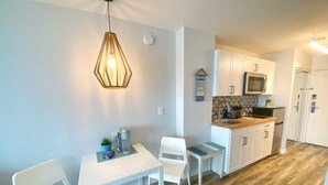 A modern kitchen with white cabinets, a microwave, and a tiled backsplash. There is a dining area with a white table and chairs, and a blue chair.