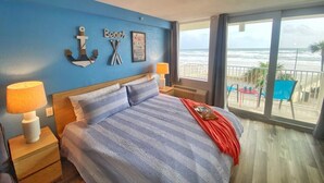 A bedroom with a large bed, a view of the beach, and a balcony with chairs.
