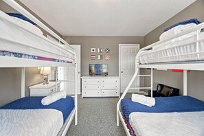 A room with bunk beds, a dresser, a desk, and a wall with flags. - Reality Check | Private Pool and Hot Tub | Sailfish Beach Access (Corolla)