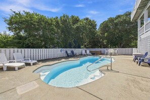 Ein Pool mit geschwungener Kante, umgeben von Liegestühlen und einem Holzzaun.