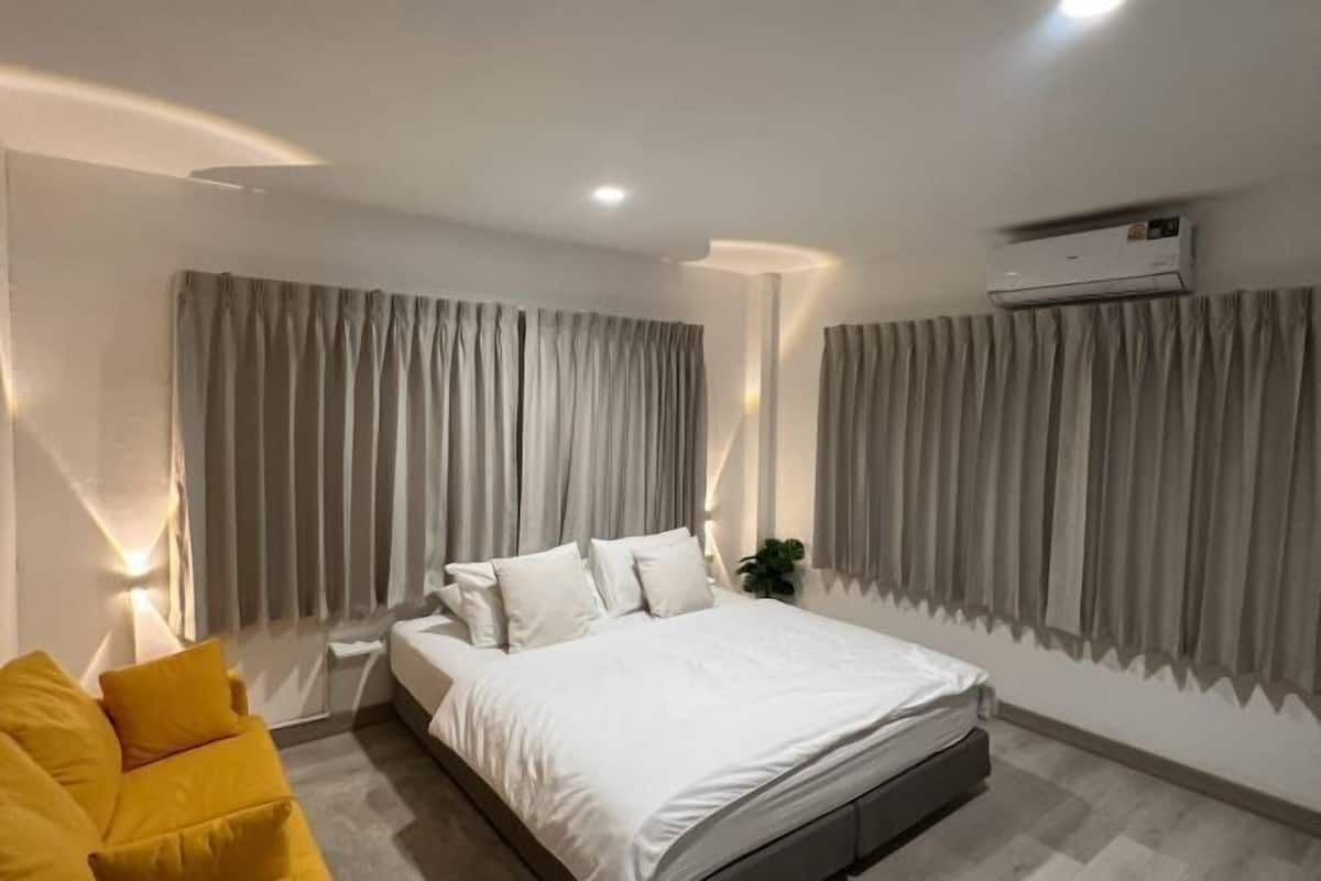 A modern bedroom with a bed, curtains, an air conditioning unit, and a sofa.