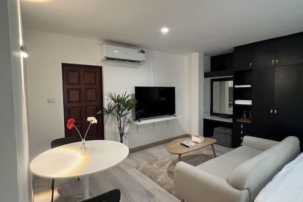 A modern living room with a sofa, a coffee table, a TV, and a dining area with a table and chairs. - Hotel Nanon Sathorn (Bangkok)