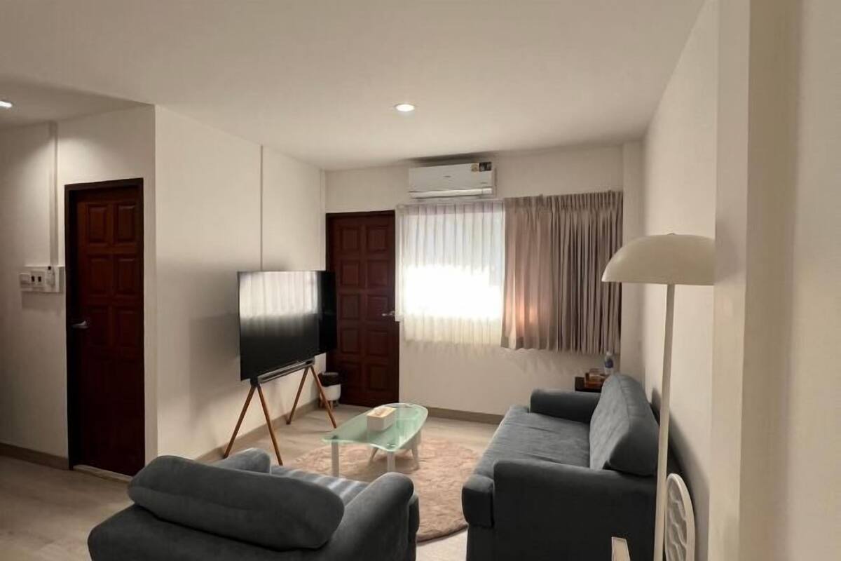 A living room with a sofa, a glass coffee table, a TV on a stand, an air conditioner, and a lamp.