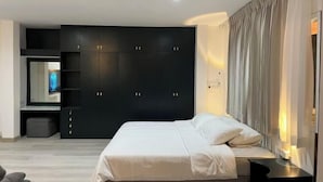Een moderne slaapkamer met een groot bed, een donkere garderobe, een televisie en een nachtkastje.
