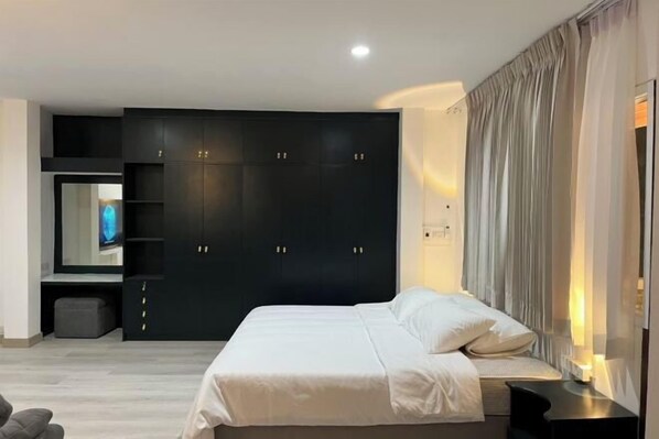 A modern bedroom with a large bed, a dark wardrobe, a TV, and a bedside table.