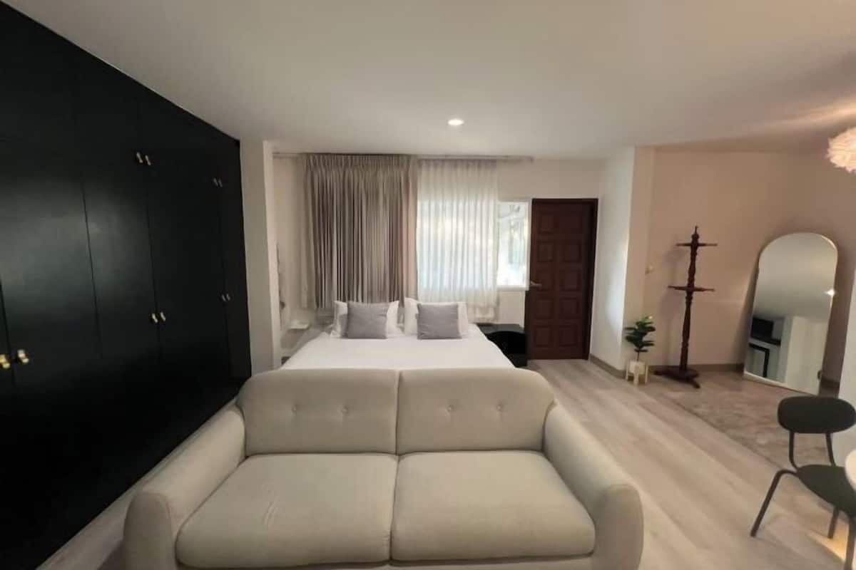 A bedroom with a bed, a sofa, a wardrobe, a mirror, and a small plant.