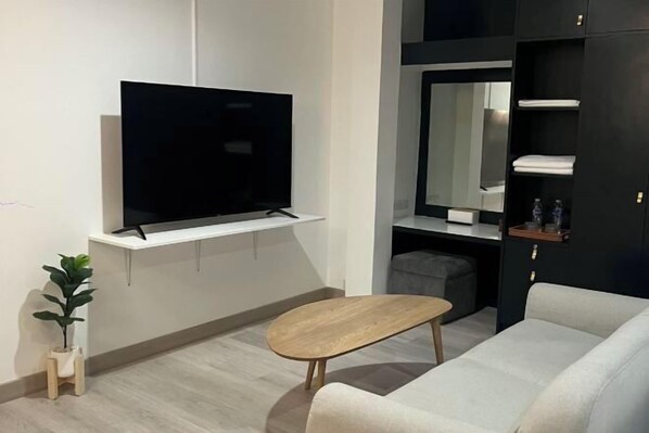 A modern living room with a flat-screen TV, a wooden coffee table, a sofa, a small plant, and built-in shelves with towels.