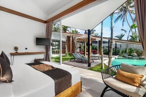 Habitación de hotel con cama, televisor, escritorio y vista a una piscina y zona exterior.