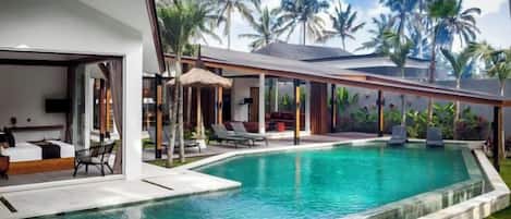 A modern poolside area with a clear pool, lounge chairs, and a covered seating area.