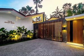 A villa with a gated entrance, a paved driveway, and a well-maintained garden with tropical plants. - Villa Crazy Roof by BaliSuperHost (Bali)