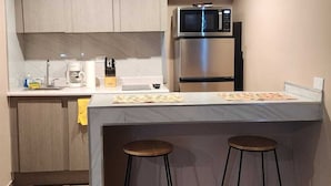Eine kleine Küche mit Mikrowelle, Kaffeemaschine und zwei Barhocker.