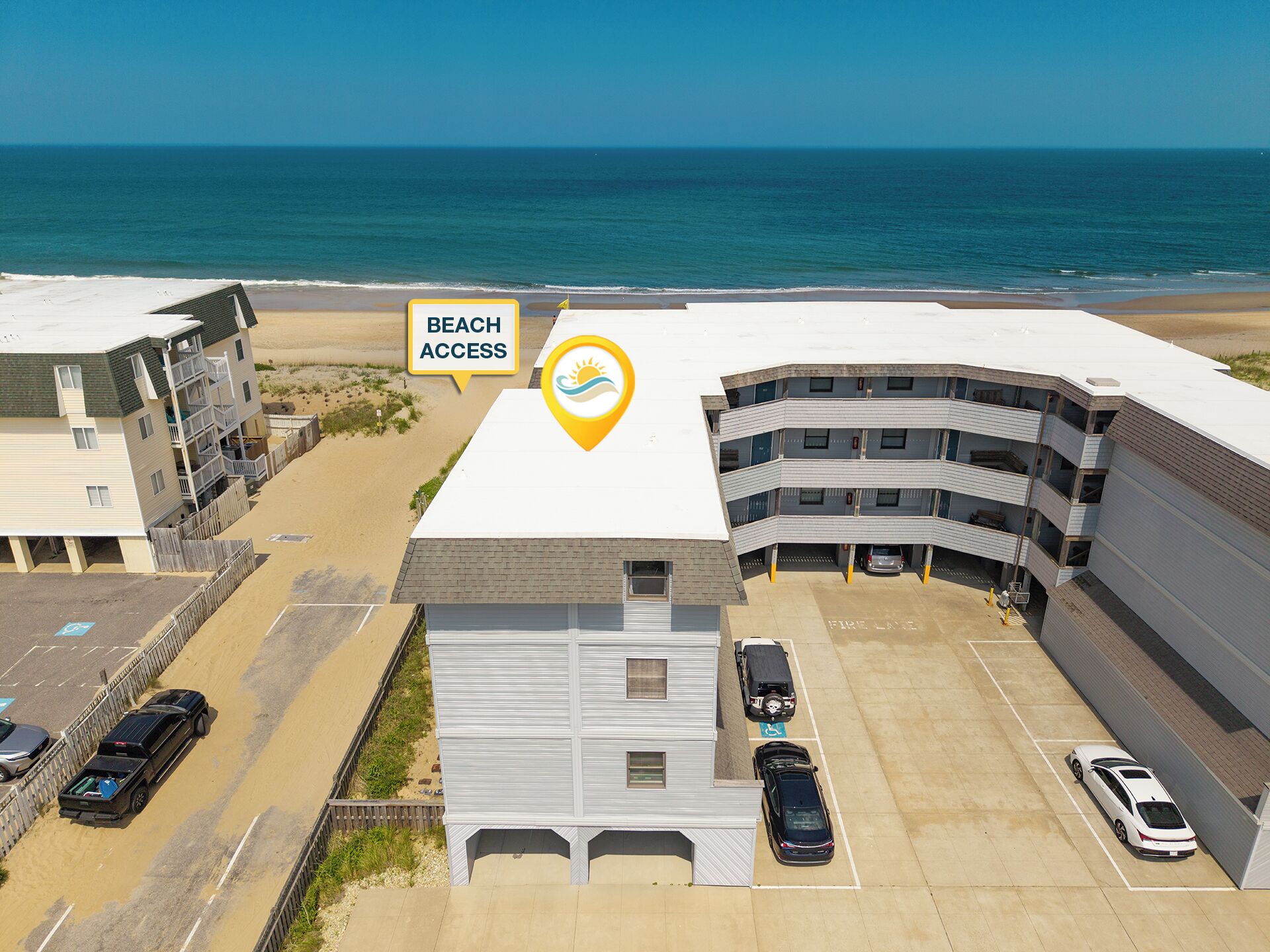 Een meerlaags gebouw met een bord dat toegang tot het strand aangeeft, parkeerplaatsen en uitzicht op de oceaan.