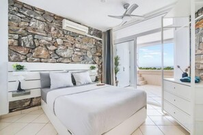 A bedroom with a stone wall, a bed, a ceiling fan, and a view of the outdoors. - Excelsior I Casa LEX Ocean&Sunrise Views Steps to Beach&Dunes Terrace Pool (Playa del Ingles)
