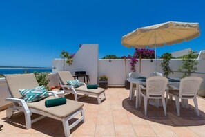 A terrace with white lounge chairs, a table with chairs, and a large umbrella. - Excelsior I Casa LEX Ocean&Sunrise Views Steps to Beach&Dunes Terrace Pool (Playa del Ingles)
