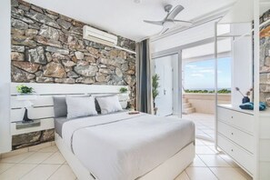 A bedroom with a stone wall, a bed, a ceiling fan, and a view of the outdoors. - Excelsior I Casa LEX Ocean&Sunrise Views Steps to Beach&Dunes Terrace Pool (Playa del Ingles)