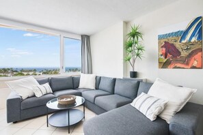 A modern living room with a sectional sofa, a small round table, and a large window offering a view of the sea. - Excelsior I Casa LEX Ocean&Sunrise Views Steps to Beach&Dunes Terrace Pool (Playa del Ingles)