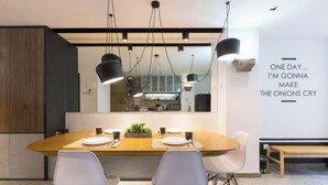 A modern dining area with a wooden table, white chairs, pendant lighting, and a kitchen in the background. - RumahKu Georgetown (George Town)
