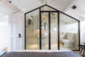 A bedroom with a bed, a white door, and a bathroom visible through a glass partition. - RumahKu Georgetown (George Town)