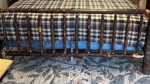 Cama com colcha xadrez e almofadas a combinar, com duas mesas de cabeceira e abajures de cada lado.