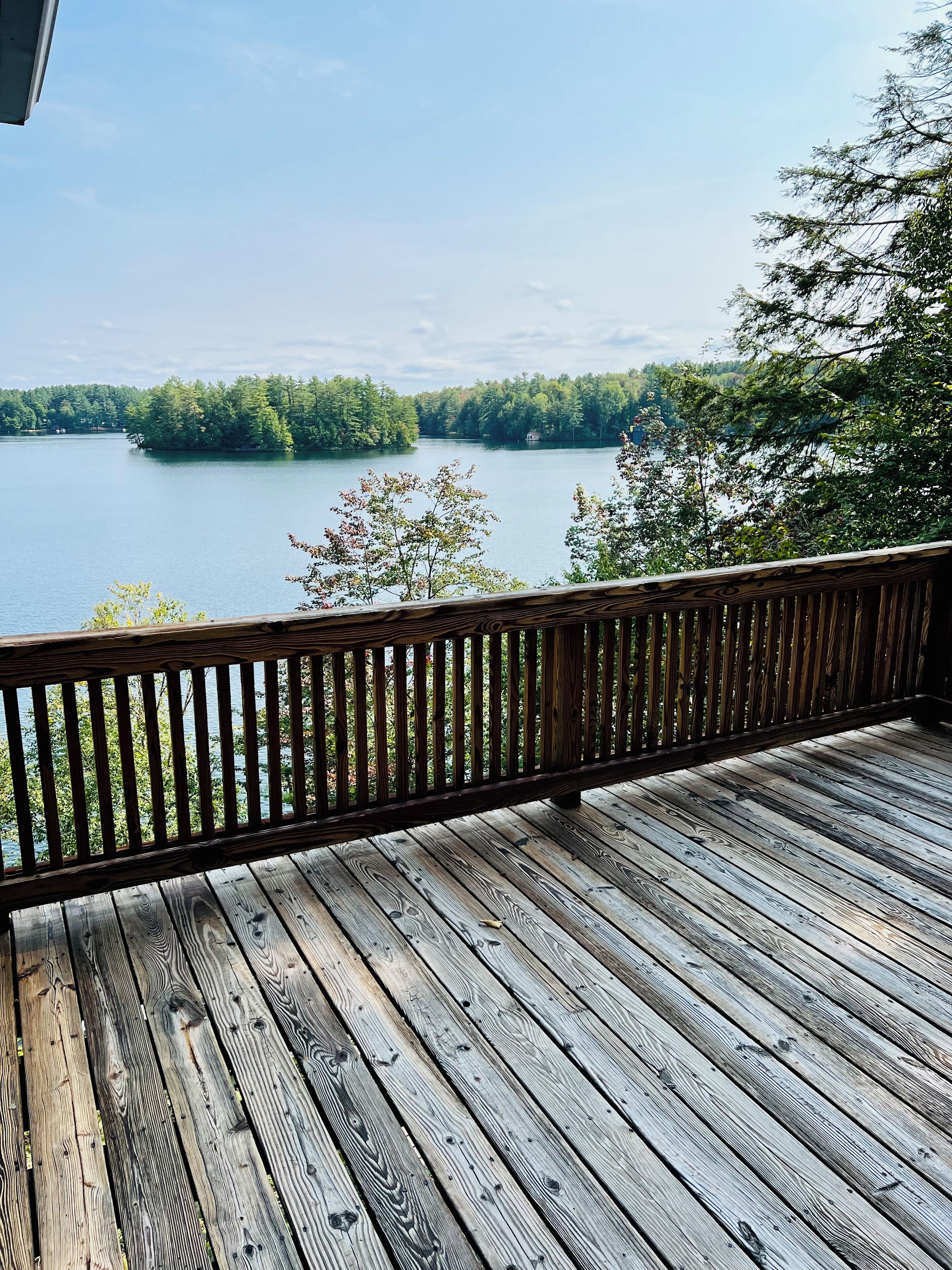 A wooden deck with a railing overlooking a lake surrounded by trees.