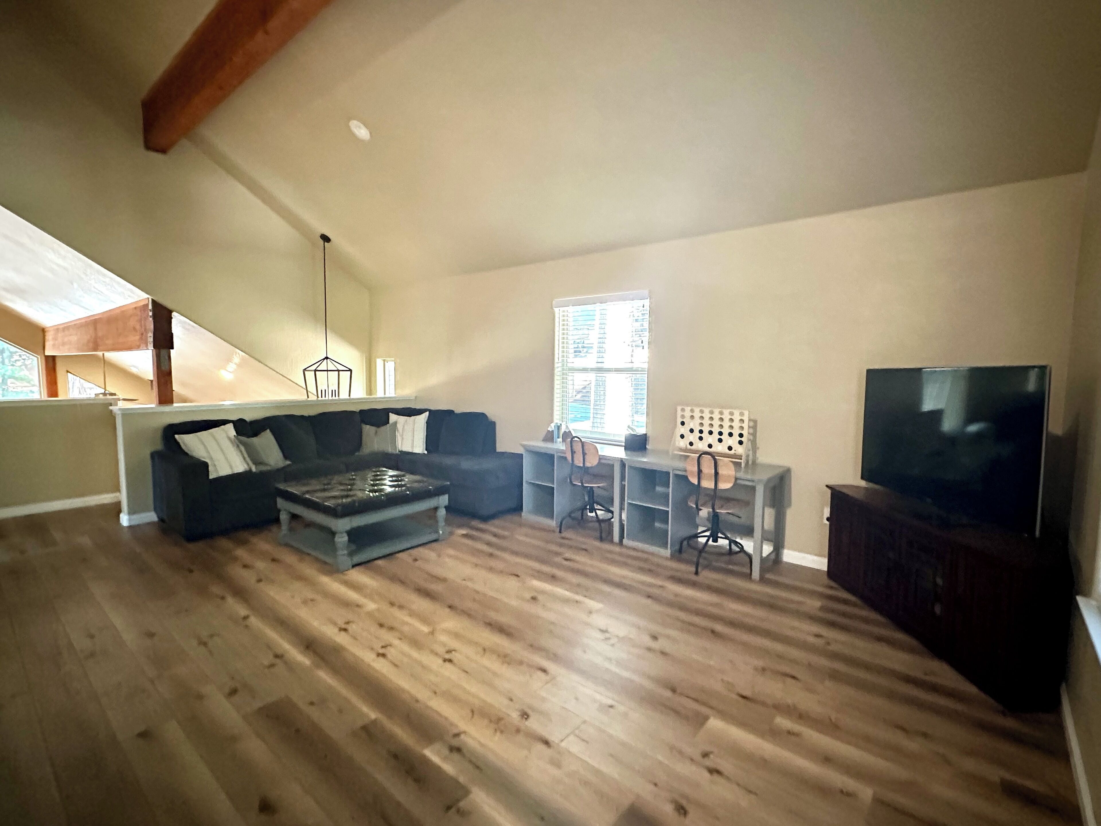 A spacious living area with a wooden floor, a sofa, a coffee table, a TV, and a dining table with chairs.