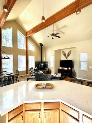 A spacious living area with a large central island, wooden ceiling beams, and a fireplace.