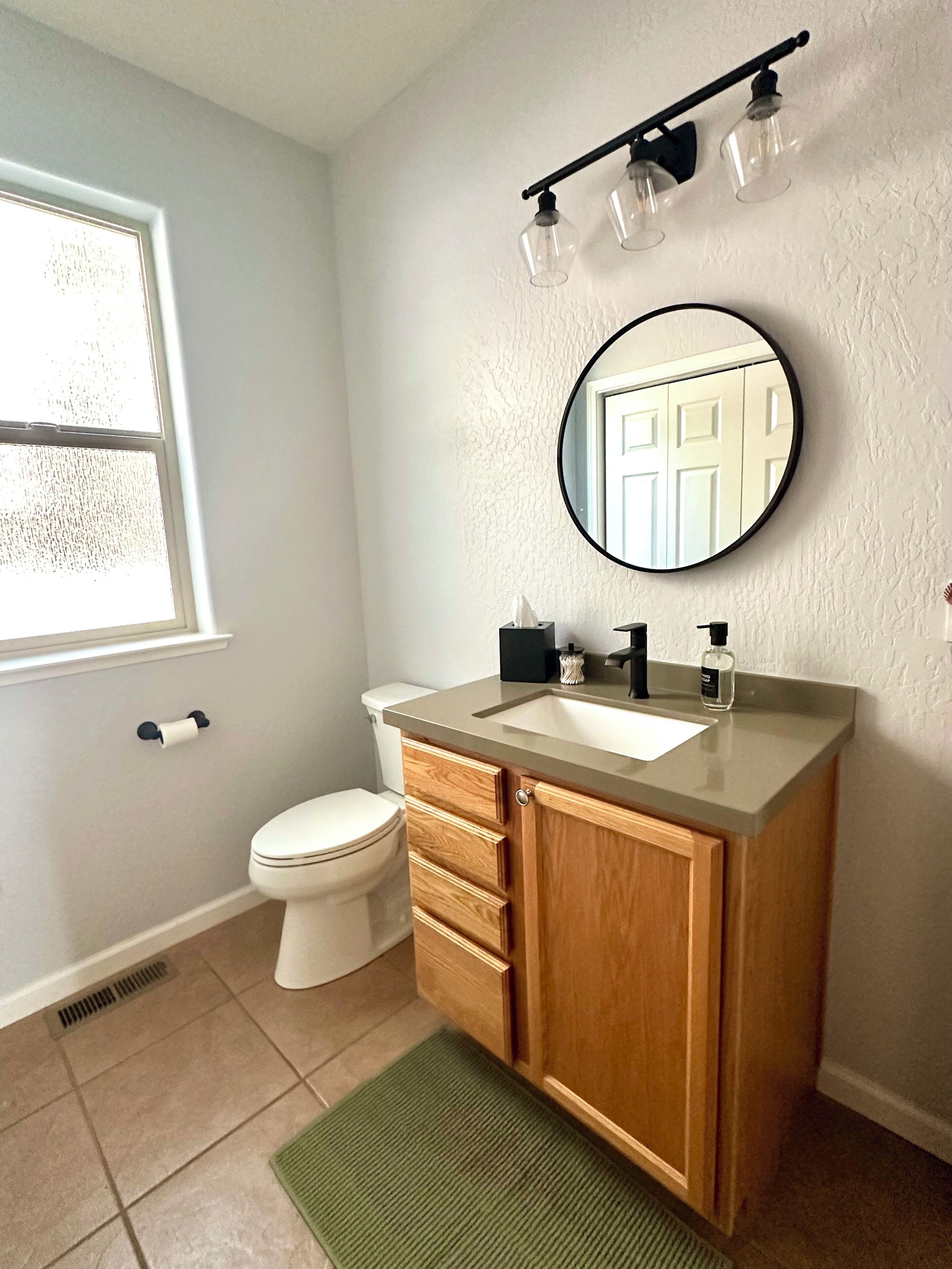 A bathroom with a toilet, sink, vanity, and a mirror.