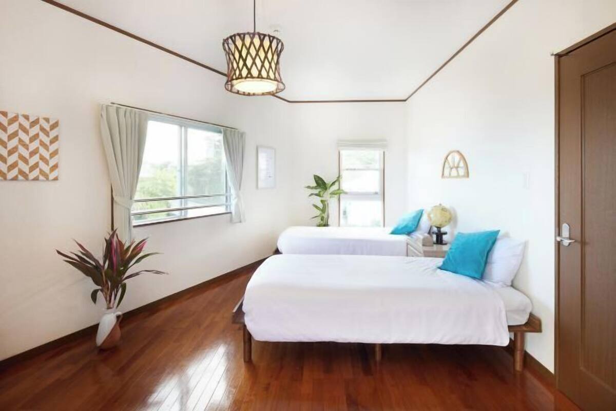 A bedroom with two beds, a potted plant, a globe, and a window with curtains.