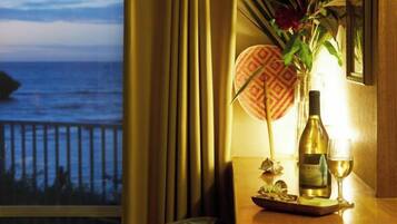 A table with a bottle of wine, a glass, and a decorative item near a window overlooking the sea.
