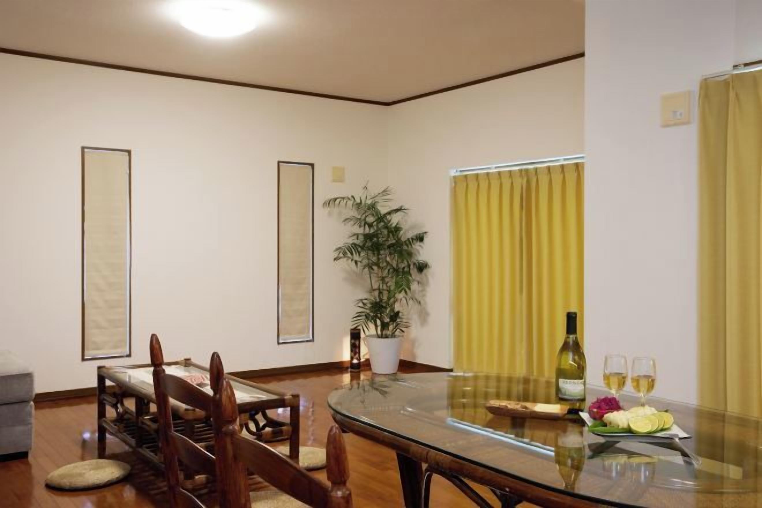 A dining area with a glass table, chairs, a potted plant, and a bottle of wine.