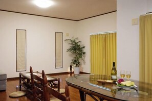 A dining area with a glass table, chairs, a potted plant, and a bottle of wine. - Ocean Therapy House (Onna)