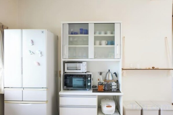 A compact kitchen with a white refrigerator, a microwave, and a cabinet with glass doors. - Ocean Therapy House (Onna)