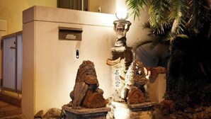 A stone lion statue in a courtyard with a palm tree and a building in the background. - Ocean Therapy House (Onna)