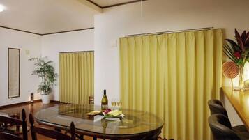 A dining area with a round glass table, chairs, a potted plant, and a curtain.