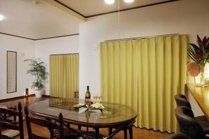 Un comedor con una mesa redonda de vidrio, sillas, una planta en maceta y una cortina.