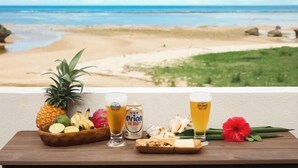 A table with a pineapple, bananas, a drink labeled 'Orion The Draft', and a flower on a balcony overlooking a beach. - Ocean Therapy House (Onna)