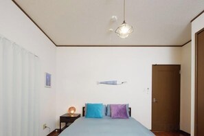 A bedroom with a bed, a bedside table with a lamp, a hanging light fixture, and a door. - Ocean Therapy House (Onna)