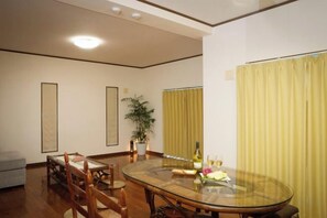 A dining area with a round glass table, chairs, a potted plant, and yellow curtains. - Ocean Therapy House (Onna)
