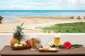 A table with a pineapple, a drink, and a can of beer, overlooking a beach.