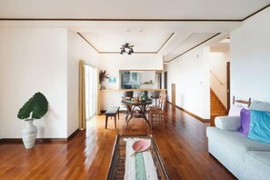 A spacious living area with a wooden floor, a dining table, and a sofa. - Ocean Therapy House (Onna)