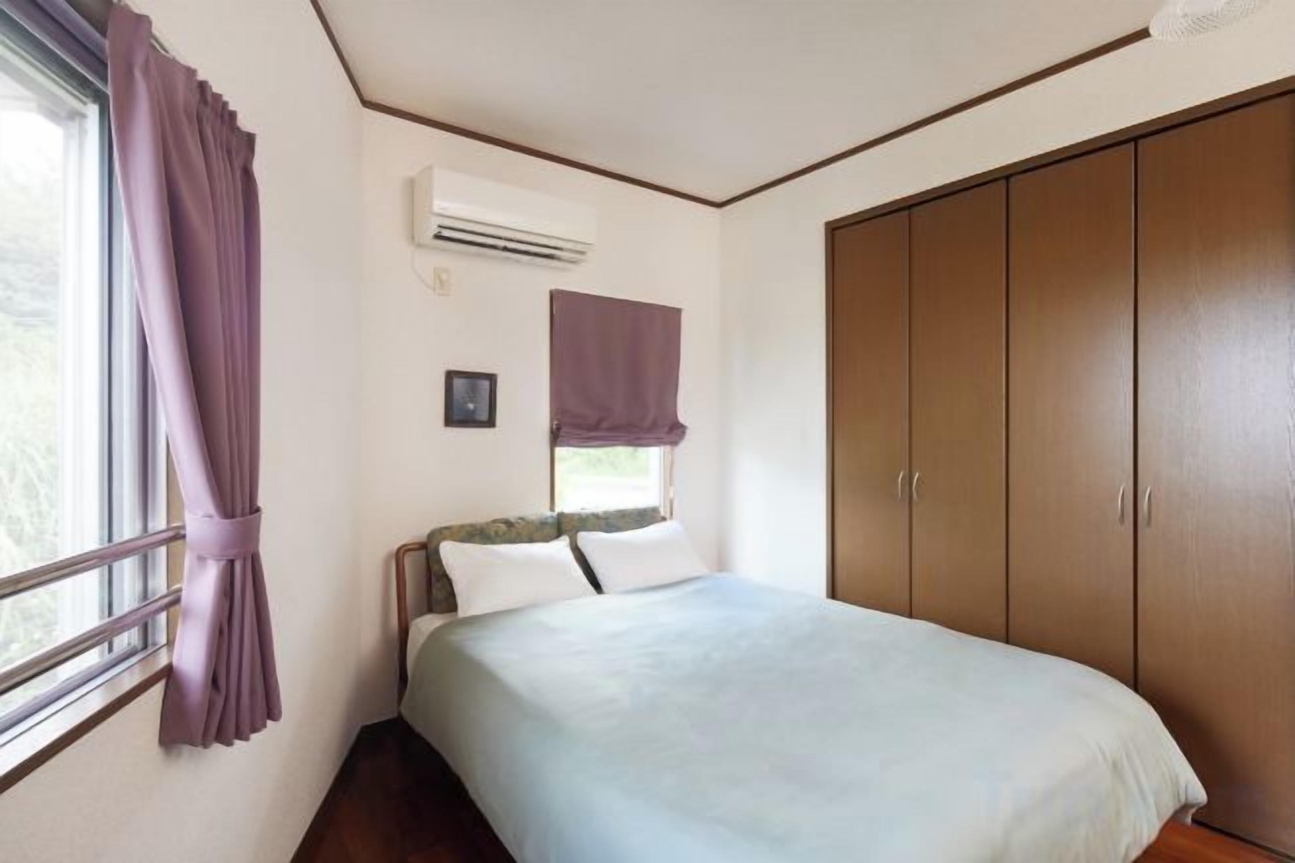 A bedroom with a bed, window, air conditioning unit, and wardrobe.