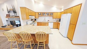 Uma cozinha moderna com armários de madeira, uma ilha central com cadeiras, forno embutido e geladeira.