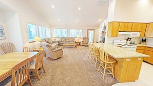A spacious living room with a large sofa set, a dining area with wooden furniture, and a kitchen with wooden cabinets and a central island. - Mt Hood 13 - A/C, Hot Tub, 2 Suites, SHARC (Sunriver)