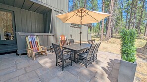 Une terrasse avec une table et des chaises, un fauteuil en bois avec des skis, et un grand parasol.