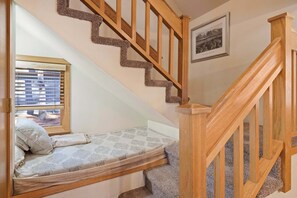 Un dormitorio con cama empotrada, ventana con persianas, una escalera de madera y un cuadro enmarcado en la pared.