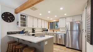 A modern kitchen with a central island, bar stools, stainless steel appliances, and a wall clock.
