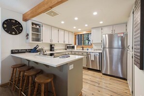 A modern kitchen with a central island, bar stools, stainless steel appliances, and a wall clock. - Otter 8- SO Close to SHARC! Updated, Hot Tub, SHARC, A/C (Sunriver)