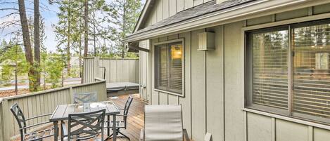 A covered patio with a table and chairs, a cushioned lounge chair, and a wooden deck.