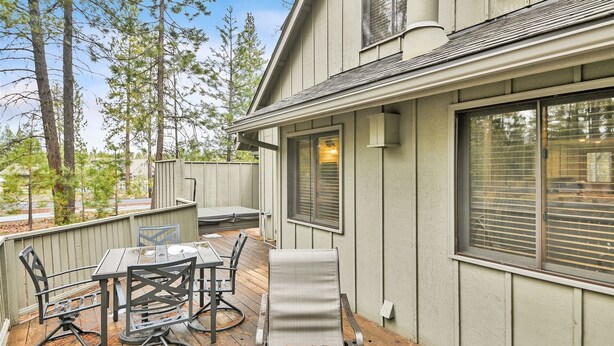 A covered patio with a table and chairs, a cushioned lounge chair, and a wooden deck.